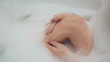 girls hands wash and caress her knees on her feet in the foam bath close-up. Slow motion