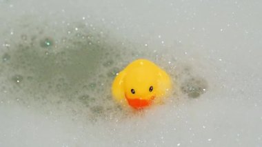 rubber yellow duck toy floats in water in bath with foam closeup
