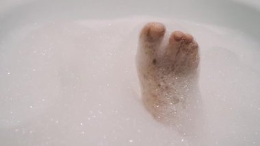 Kız parmaklarıyla köpük banyosunda oynuyor zevkle ve yavaş çekimde eğleniyor.