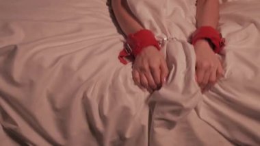 BDSM kelepçeli, elleri kelepçeli, elleri kelepçeli, sert seks ve orgazm olmuş bir kadın gece yatağa beyaz bir çarşaf seriyor.