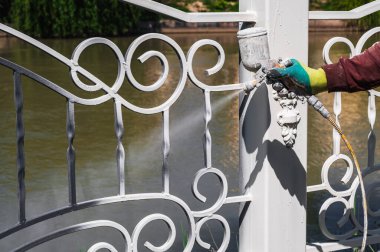 Bir işçinin eline sprey tabancayla beyaza boyanmış metal bir çit.