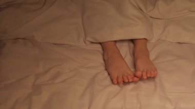 Çocuk ayaklar gece çarşafın üzerinde battaniyenin altında. Çıplak ayaklı uyuyan küçük kız. Yatak odasındaki rahat bir yatakta uykusunda sallanıyor.