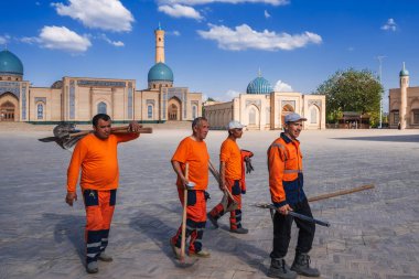 group of Uzbek male janitors in orange uniforms with shovels on the street in spring on square of the Hazrati Imam architectural complex. Tashkent, Uzbekistan - April 17, 2024 clipart