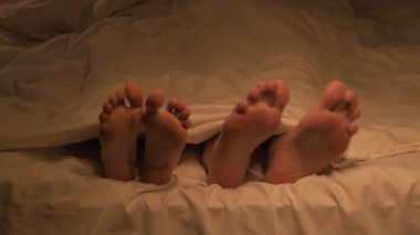 Yataktaki yatak odasında yorganın altında dans eden birkaç kadın ve erkeğin mutlu bacaklarını oynatmak eğlenceli.