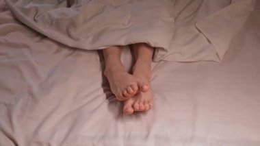 Beyaz bir çarşafın üzerinde battaniyenin altında gece rüyada hareket eden ayak parmakları olan bir kadın. Kadın kadın çıplak ayakla bir yatak odasında uyuyor.