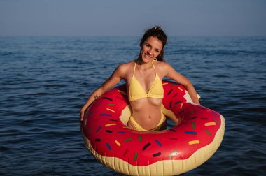 Mayo giymiş, elinde şişirilebilir bir daire olan mutlu ve genç bir kadın güneşli bir yaz gününde denizde dinleniyor.
