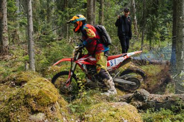 KARELİYA, RUSSIA REÜKLİK - CIRCA HAZİRAN 2022: Karelia 'da Ladoga Kupası 2022 off-road turnuvası. Bir motosiklet sürücüsü, bir motokros yarışında, engebeli bir ormanın içinden geçen bir spor motosikleti kullanıyor.