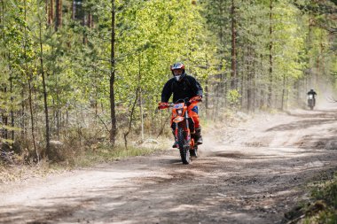 KARELİYA, RUSSIA REÜKLİK - CIRCA HAZİRAN 2022: Karelia 'da Ladoga Kupası 2022 off-road turnuvası. Spora dayanıklı motosiklet süren motosikletli motosiklet sürücüsü ormanın tozlu yollarında motosiklet yarışı yapıyor.
