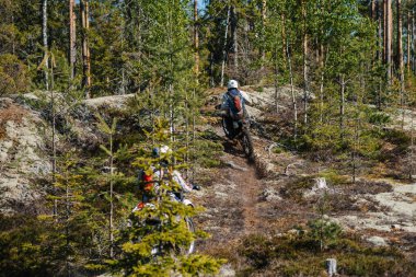 KARELİYA, RUSSIA REÜKLİK - CIRCA HAZİRAN 2022: Karelia 'da Ladoga Kupası 2022 off-road turnuvası. Motosiklet yarışçısı motorsikletle dağlarda motorsiklet sürerken ormanın içinden Motokros yarışmasında