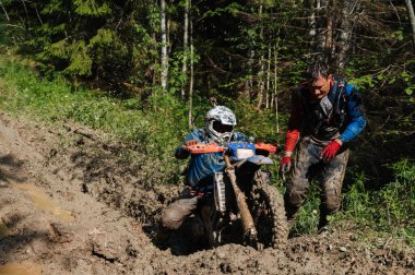KARELİYA, RUSSIA REÜKLİK - CIRCA HAZİRAN 2022: Karelia 'da Ladoga Kupası 2022 off-road turnuvası. Kirli motosiklet yarışçıları, motokros yarışmasında Forest Road 'da çamurdan bir spor motosikleti çıkarıyorlar.