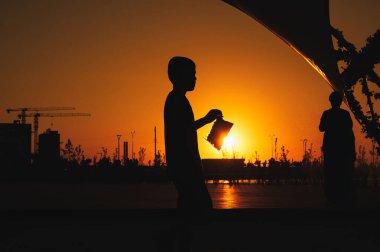 Gün batımında halka açık bir parkta eğlenen insanların siluetleri..