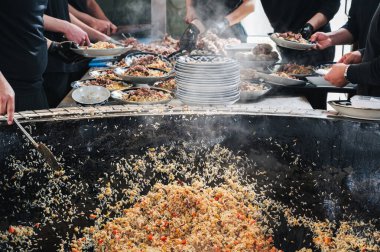 Erkek şefler, restoranın mutfağındaki kazanda sebzeli Özbek pilavı pişiriyor. Geleneksel Asya mutfağı. Özbekistan 'daki Pilaf Merkezi, Taşkent