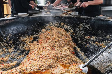 Erkek şefler, restoranın mutfağındaki büyük bir kazanda Özbek pilavı pişiriyor. Geleneksel doğu mutfağı. Orta Asya Pilaf Merkezi Besh Qozon, Özbekistan, Taşkent