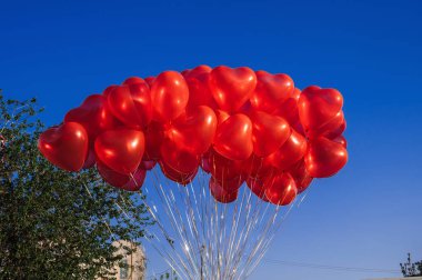 Mavi gökyüzünün arka planında kalp şeklinde bir sürü kırmızı balon var.