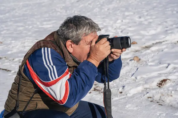 Elinde kamera olan yaşlı bir adam, bir dağ kışı manzarasını fotoğraflıyor..