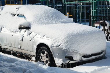 Otoparka karla kaplı bir araba park edildi. Arabanın lastikleri, tekerlekleri ve kaputu beyaz bir kaplamayla kaplı.