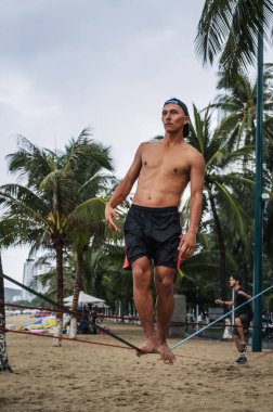 Genç bir adam yaz aylarında sahilde ip üzerinde yürümek için antrenman yapar. Nha Trang, Vietnam - 29 Temmuz 2024