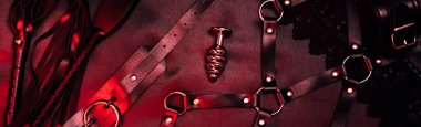 set of BDSM sex toys with handcuffs, whip flogger, butt anal plug for submission on a red background. Wide header cover for banner for sex shop