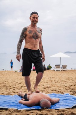 Yaz tatilinde sahilde yatan bir adamın sırtına ayak masajı yapan bir adam. Nha Trang, Vietnam - 25 Temmuz 2024