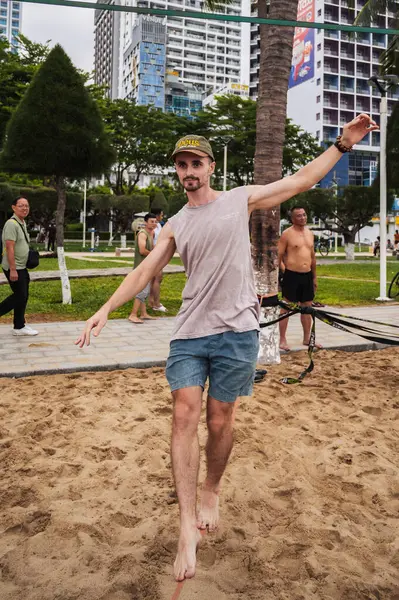 stock image A male acrobat in slackline training walks a tightrope on the beach in summer. Nha Trang, Vietnam - July 25, 2024