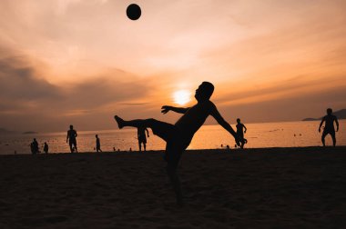 Gün batımında deniz kenarında top oynayan Vietnamlı erkeklerin siluetleri. Nha Trang, Vietnam - 31 Temmuz 2024