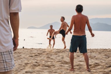 Adult Asian men play beach soccer on the beach by the sea in summer. Nha Trang, Vietnam - July 31, 2024 clipart