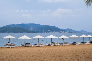 Yaz bulutlu bir günde Vietnam 'da Nha Trang tatil köyünde plaj şemsiyelerinin altında dinlenen turistlerle dolu kumlu bir sahil.