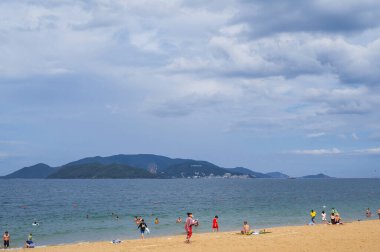 Vietnam 'ın Nha Trang tatil beldesinde deniz kenarında turistlerin olduğu kumlu bir sahil. Yazın VinPearl Adası' na bakıyor. Nha Trang, Vietnam - 22 Temmuz 2024