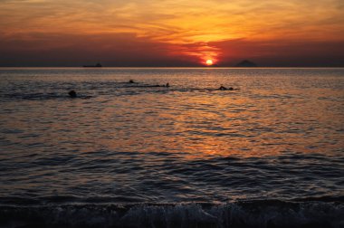 Yazın gün doğumunda bir tatil köyünde yüzen insanların siluetleri.