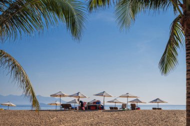 Yazın Asya 'da tropikal bir tatil köyünde deniz kenarında palmiye ağaçları olan kumlu bir sahilde güneşli şemsiyeler. Nha Trang, Vietnam - 3 Ağustos 2024