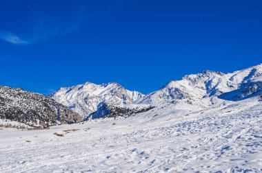 Gün boyunca mavi gökyüzünün altında karla kaplı dağlarla kaplı kış manzarası