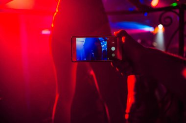 mans hand with a smartphone takes pictures of a dancers ass in a nightclub