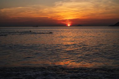 Yazın gün doğumunda bir tatil köyünde yüzen insanların siluetleri.