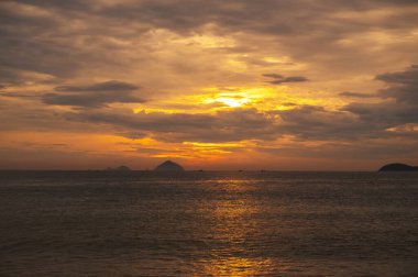 Yazın gün batımında, turuncu gökyüzünün arka planında adaları olan bir deniz.