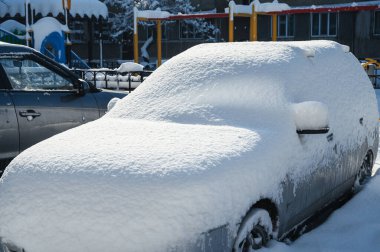 Bir kar yağışı sonrası park etmiş bir araba karla kaplıdır..