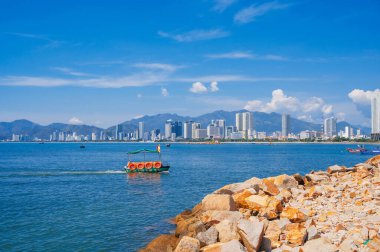 Sahilin arka planında büyük kayalar, Vietnam tekneleri, dağlar ve Nha Trang, Vietnam 'daki yüksek binalar.
