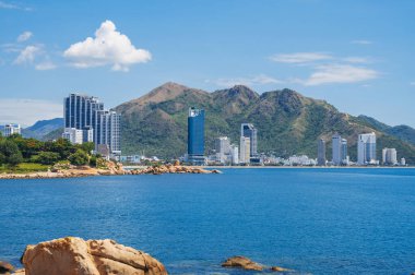 Large rocks on the background of the beach, mountains and high-rise buildings in Nha Trang, Vietnam clipart