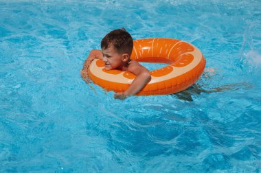Şişme dairedeki küçük çocuk yaz tatilinde bir otelin havuzunda yüzmeyi öğreniyor.
