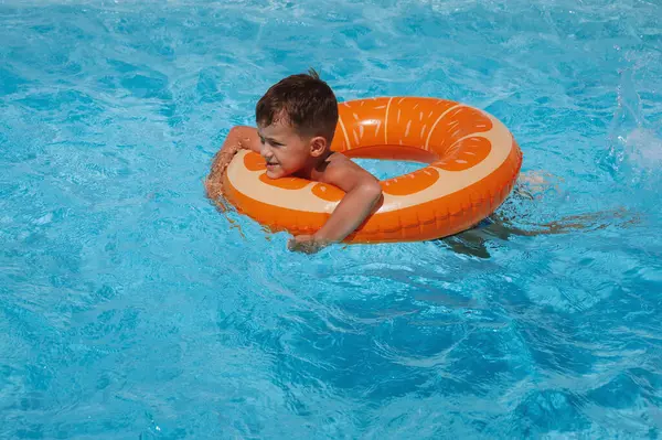 Şişme dairedeki küçük çocuk yaz tatilinde bir otelin havuzunda yüzmeyi öğreniyor.