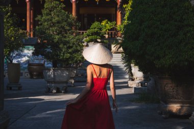 Kırmızı elbiseli genç kadın turist ve geleneksel Vietnam şapkası Non La Vietnam 'daki bir pagoda' da Asya 'ya seyahat ederken.