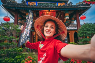 Vietnam 'da Asya' da bir tapınakta Vietnamlı şapkalı mutlu genç bir kadın turistin selfie portresi.