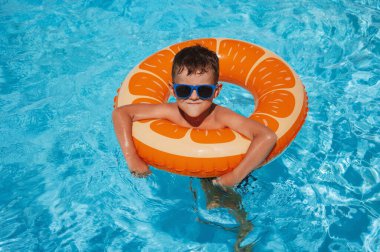 Şişme çemberdeki çocuk yaz tatilinde bir otelin havuzunda yüzmeyi öğreniyor.