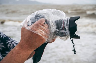 Su geçirmez çantadaki dijital kamera ve yağmura karşı koruyucu plastik torba bir fotoğrafçının erkek ellerine sıçrıyor.
