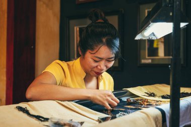 Mutlu Vietnamlı kadın nakışçı, Asya 'nın Hoi An şehrindeki bir atölyede ipek bir tablo işliyor. Hoi An, Vietnam - 1 Aralık 2024