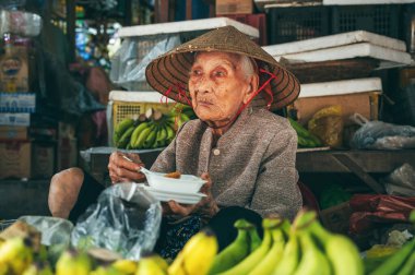 Vietnam 'da Hoi An' da bir caddedeki Asya gıda pazarında meyve satan yaşlı Vietnamlı bir kadının portresi. Hoi An, Vietnam - 1 Aralık 2024