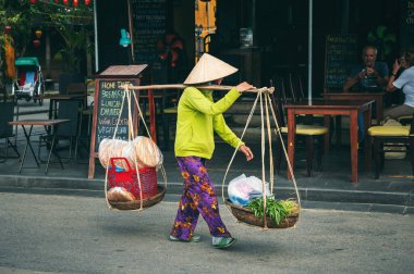 Geleneksel Non La şapkalı Vietnamlı kadın satıcı, Asya 'da Vietnam' da Hoi An şehrinin sokaklarında sepetlerde yiyecek satıyor. Hoi An, Vietnam - 2 Aralık 2024