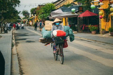 Vietnamlı yaşlı bir kadın Vietnam 'da Hoi An şehrinde çöp ve mukavva ile bisiklet sürüyor. Hoi An, Vietnam - 2 Aralık 2024
