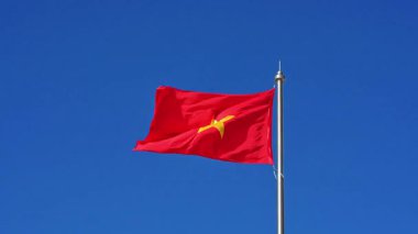Yüksek bir bayrak direğinde kırmızı Vietnam bayrağı dalgalanır rüzgarda mavi gökyüzünün arka planında