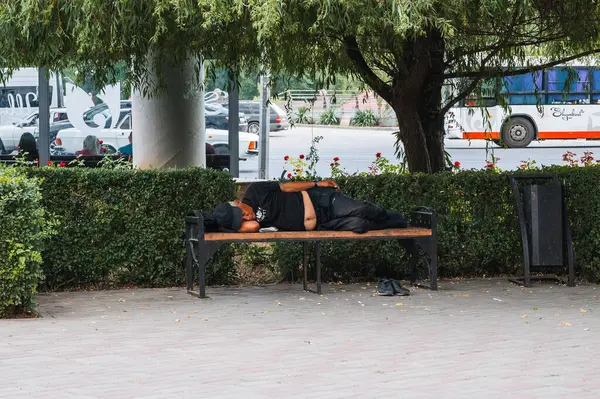 Evsiz bir adam şehirdeki bir sokakta bir bankta uyuyor. Şymkent, Kazakistan - 12 Temmuz 2024