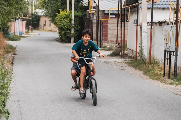 Genç bir Kazak çocuğun iki mutlu arkadaşı yaz tatilinde bisiklet sürerler. Şymkent, Kazakistan - 12 Temmuz 2024